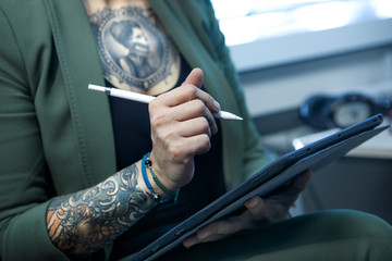 Dettaglio di mano con pencil digitale di  Manager donna tatuata bionda, vestita con una giacca...
