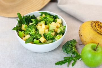 tarelka zelenogo salata s brokkoli, yablokom, rukkoloy i repkoy na serom fone. Svezhaya, organicheskaya yeda dlya zdorovogo obraza zhizni, pokhudeniya, detoksa, keton diyety. Zavtrak fermera repa