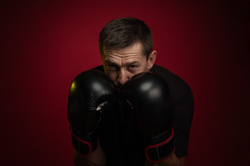 Male athlete boxer with gloves in his hands posing against a dark red background