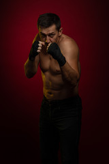 Obraz na płótnie Canvas Male athlete boxer with gloves in his hands posing against a dark red background