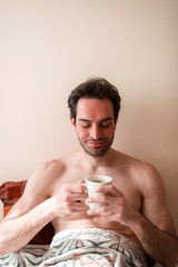 In the morning, handsome male in his bedroom with cup of tea or coffee