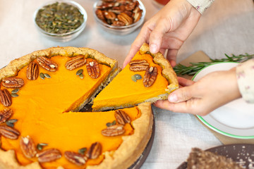  woman cuts a piece of pumpkin pie and puts it on a plate. Autumn family dinner. Homemade sweet cake. Traditional festive dessert.