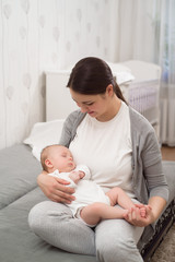 Young mother holding her newborn child. Mom nursing baby. Woman and new born boy relax in a white bedroom.