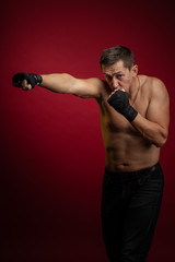 Fototapeta na wymiar Male athlete boxer with gloves in his hands posing against a dark red background