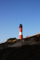 Red and white lighthouse on the island, blue sky background
