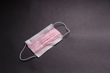 One disposable pinkish medical face mask on a black background. Horizontal view.