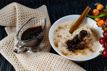 Sour-milk yogurt dessert, with thermostatic cooking, decorated with ripe cherry berries in syrup, on a dark background with jam in sauce and a stick of cinnamon, next to sprigs of fresh red berries
