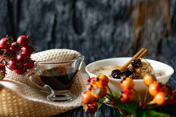 Sour-milk yogurt dessert, with thermostatic cooking, decorated with ripe cherry berries in syrup, on a dark background with jam in sauce and a stick of cinnamon, next to sprigs of fresh red berries