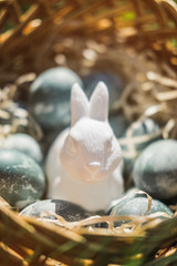 Painted blue textured easter eggs and a white plastic rabbit in a wicker brown hand made basket on green fresh grass. The concept of the spring holiday and egg hunting.