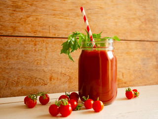 Tomato juice with fresh celery and straw in a jar and fresh cherry tomato on a wooden table.