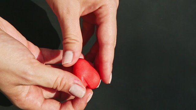 top view closeup hands form heart shaped from small piece of red marzipan mass