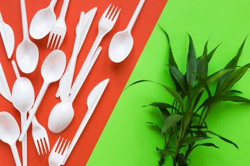 White disposable spoons, forks, knives and tree on red and green background close-up - Environmental problem concept