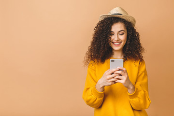 Portrait of a smiling casual curly student woman holding smartphone isolated over beige background.