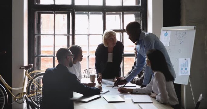 Focused mature businesswoman explaining new project plan to youn african american employee at diverse colleagues brainstorming meeting. Multiracial teammates working together on company strategy.