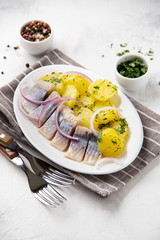 Pickled herring fillet in oil with potatoes, red onions and herbs, flavorful fish, Russian appetizer, traditional food