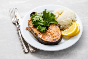 fried salmon with boiled rice, salad and lemon on white plate
