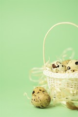 White wicker basket filled with straw,quail eggs on a green background. The concept of Easter Holidays. Easter card.Copy space.