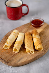 Crepes with raspberry jam on a wooden board. Golden pancakes with a coffee perfect breakfast....