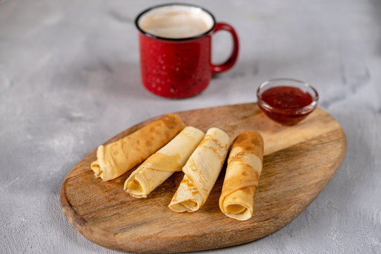 Crepes with raspberry jam on a wooden board. Golden pancakes with a coffee perfect breakfast. Serving of russian blin on a gray background.