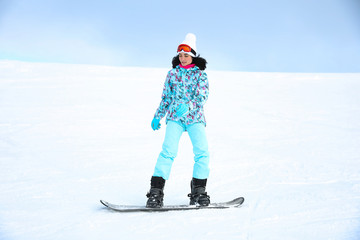 Young woman snowboarding on hill at mountain resort. Winter vacation