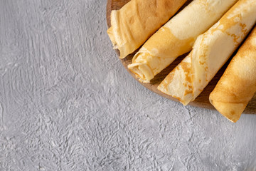 Golden crepes on a wooden board top view. Breakfast time. Serving of pancakes on a gray background.