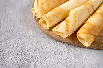 Golden crepes on a wooden board. Breakfast time. Serving of pancakes on a gray background.