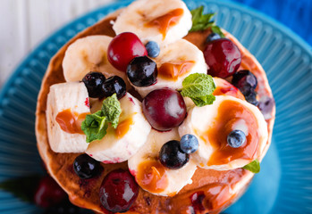 Delicious pancakes with banana, berries, mint and salted caramel in a plate.