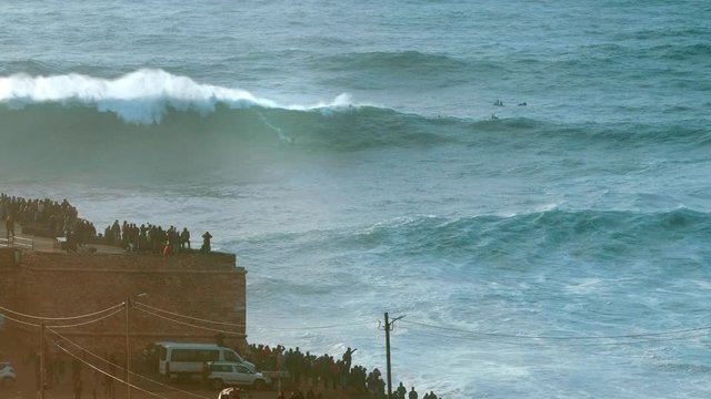 NAZARE, PORTUGAL - DECEMBER 22, 2019:  Amazing shot of a jetski pushing a big wave surfer to ride a massive wave in Nazare, Portugal. People are watching dangerous surfing: a popular tourist spot and 
