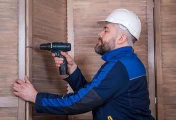 a bearded man carpenter with a screwdriver in his hands is assembling wooden louver panels