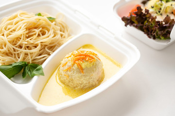 food delivery in white lunch boxes. Food to go. Meatballs in sauce and pasta.