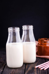 Obraz na płótnie Canvas Two bottles of fresh milk with tubes and fresh homemade salted caramel n dark background.