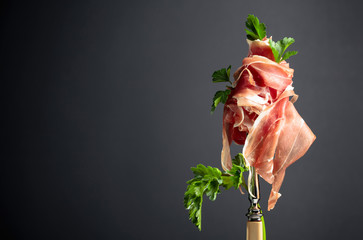 Thin sliced prosciutto with parsley on a fork. Traditional Italian cuisine.