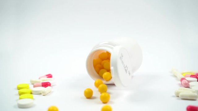 Yellow Pills fall out of bottle slow motion. Tablets and vitamins on  white background. Vitamin C, medications.