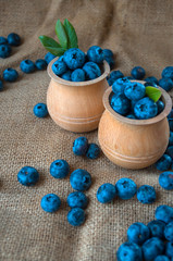 Fresh organic blueberries in a wooden bowl on a sackcloth background. Juicy and fresh blueberries with green leaves on rustic table. Bilberry on wooden Background. Blueberry antioxidant