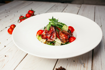 Vegetable salad with meat and barbecue sauce served on a large round white plate. Restaurant dish on a wooden background.