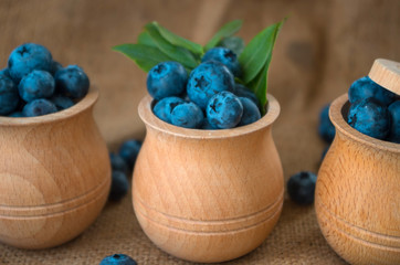 Fresh organic blueberries in a wooden bowl on a sackcloth background. Juicy and fresh blueberries with green leaves on rustic table. Bilberry on wooden Background. Blueberry antioxidant