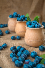 Fresh organic blueberries in wooden bowl on a sackcloth background. Juicy and fresh blueberries with green leaves on rustic table. Bilberry on wooden Background. Blueberry antioxidant