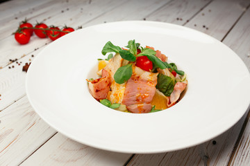 Salad of various vegetables and fresh salmon. Restaurant dish on a wooden background. The table is decorated with tomatoes and star anise.