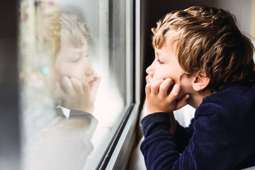 Portrait of boy looking out the window of his house bored, respecting quarantine for viruses in...
