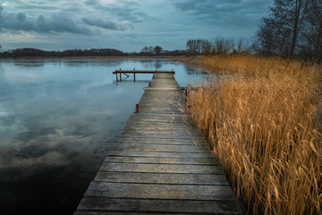 Fototapeta na wymiar A long wooden bridge and reed on the lake, dark clouds on the sky