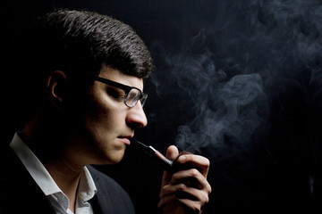 Obraz premium A young brunette smokes a pipe in the dark. Man smoking a pipe