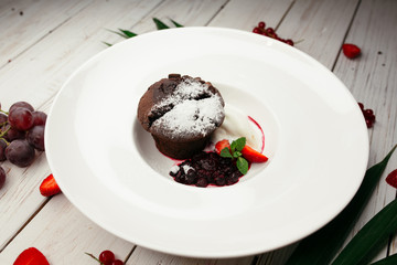 Appetizing sweet dessert on a white plate. A restaurant dish on the table decorated with strawberries and grapes.