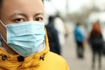 Fototapeta na wymiar Asian man wearing medical mask on city street, closeup with view space for text. Virus outbreak