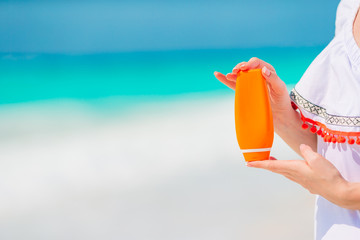 Beautiful young woman holding a suncream on tropical beach