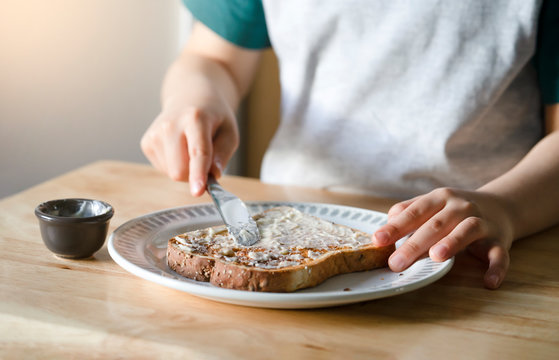 Cropped image of kid hands spreading butter on bread, Child applying butter to toast for his breakfast Kid is preparing food , Heahty life stye concept