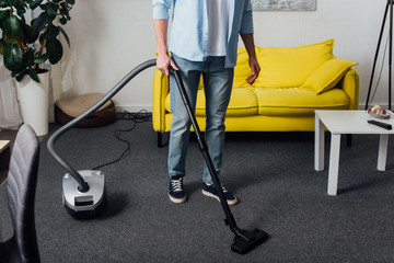 Cropped view of man using vacuum cleaner while cleaning carpet in living room