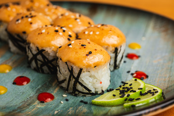 A close up of fresh maki covered with orange sauce, garnished with black sesame seeds and lime, on a blue plate