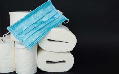 A white rolls of soft toilet paper and medical face mask on black background