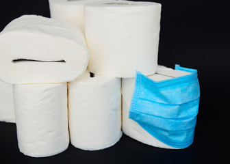 A white rolls of soft toilet paper and medical face mask on black background