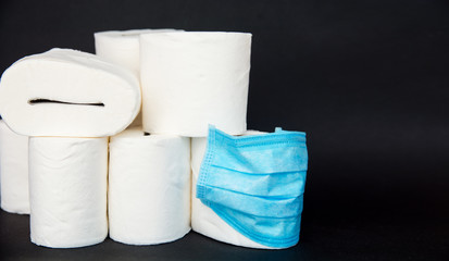 A white rolls of soft toilet paper and medical face mask on black background